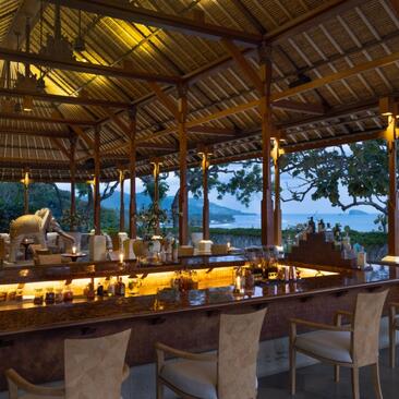 Terrasse de bar du resort Amankila au coucher du soleil, avec vue sur l'océan et architecture en bois.