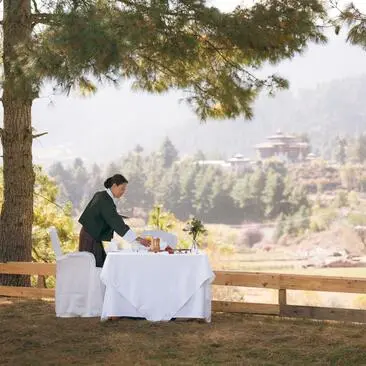 Outdoor lunch setting at Amankora's Bumthang Lodge with valley views and pine forest backdrop.