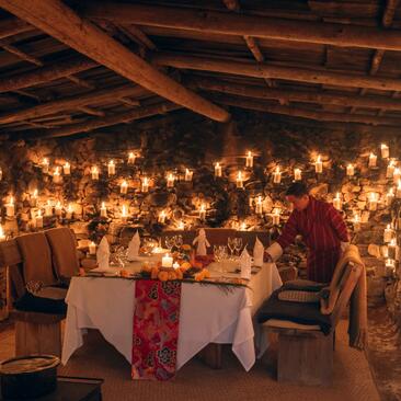 Candlelit dining room at Amankora with wooden beams and glowing lanterns overhead, two place settings prepared for dinner.