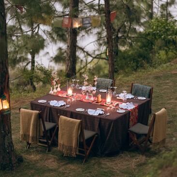 Riverside dining setup at Amankora's Punakha Lodge with candlelit table among tall trees at dusk.