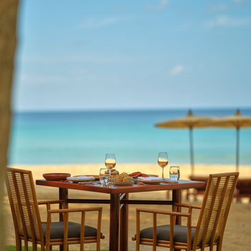 Tavolo da pranzo Nura allestito sulla spiaggia con vista sul mare presso il resort Amanpuri in Tailandia.