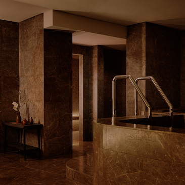 Aman Nai Lert Bangkok suite with warm-toned marble columns and a sunken plunge pool in soft lighting.