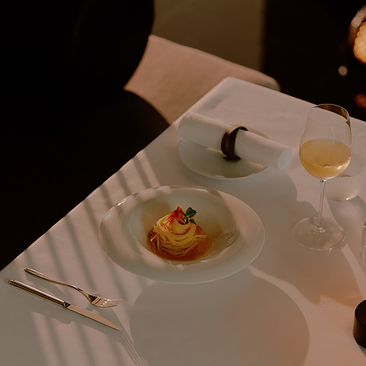 Plated dish with golden sauce and garnish at Aman Nai Lert Bangkok, accompanied by a glass of wine.