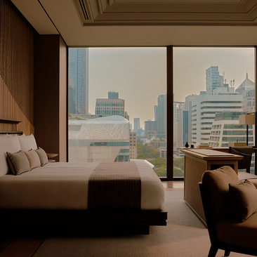 Principal bedroom at Aman Nai Lert Bangkok with floor-to-ceiling windows overlooking the city skyline.