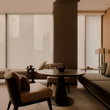 Minimalist hotel room at Aman Nai Lert Bangkok with brown leather armchair, dark column, and floor-to-ceiling windows.