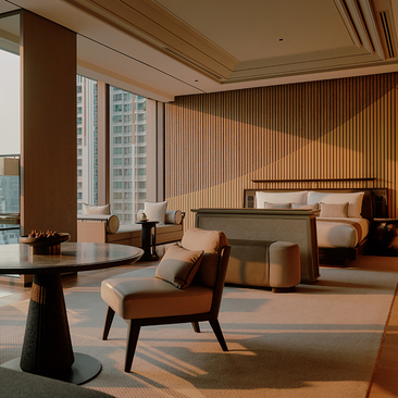 Spacious hotel bedroom at Aman Nai Lert Bangkok with warm wood tones, floor-to-ceiling windows overlooking the city, and contemporary furnishings.