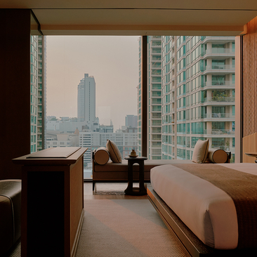 Room at Aman Nai Lert Bangkok with floor-to-ceiling windows overlooking Bangkok's skyline and modern buildings.