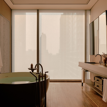 A principal bedroom at Aman Nai Lert Bangkok with a dark soaking tub and large windows overlooking the city.