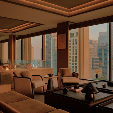Aman Suite living room at Aman Nai Lert Bangkok, with floor-to-ceiling windows overlooking the city skyline, warm wood panelling, and contemporary furnishings.