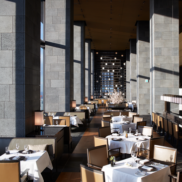 Aman Tokyo's dining venue with soaring whitewashed columns, wooden tables, and soft natural light filtering through tall windows.