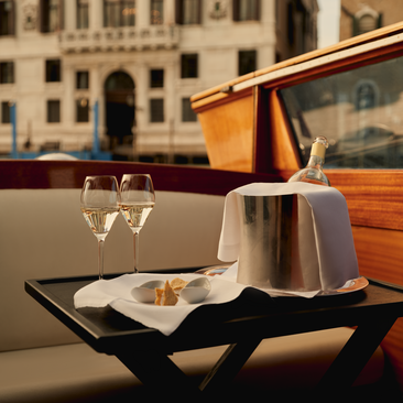 Boat aperitivo at Aman Venice with glasses and snacks on a table, Venetian palaces visible across the water.