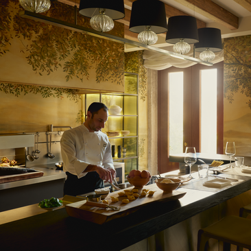 Chef preparing food in Aman Venice's Palazzo kitchen, with golden walls and natural light.