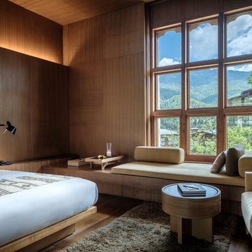 Amankora suite bedroom in Bumthang with low platform bed, wooden desk and large windows overlooking mountain landscape.