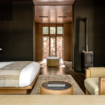 Amankora Paro Lodge suite with principal bed, circular soaking tub, and timber-framed doors opening to exterior views.
