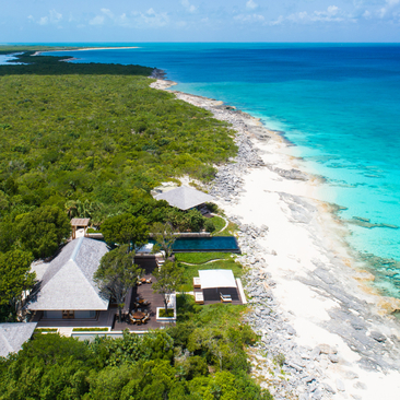 Aerial view of a five-bedroom villa at Amanyara nestled among tropical vegetation along a turquoise coastline in Turks and Caicos.