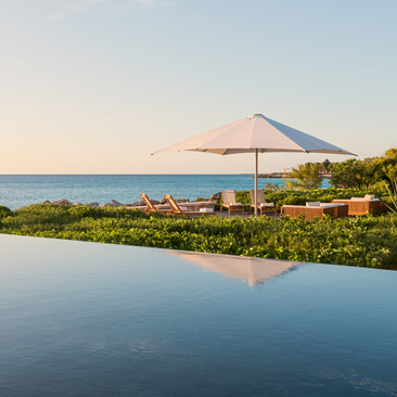 Infinity pool reflecting sky at sunset, with beachfront views of turquoise waters at Amanyara, Turks and Caicos.