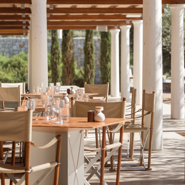 Dining terrace overlooking the Aegean at Amanzoe resort, Greece, with wooden columns and tables set for service.