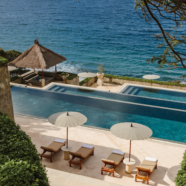 Piscine surplombant la mer à Amankila, station balnéaire avec transats et parasols.