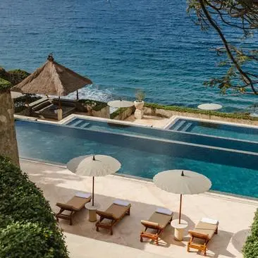 Amankila infinity pool overlooking turquoise ocean waters, with loungers and parasols on the terrace below.
