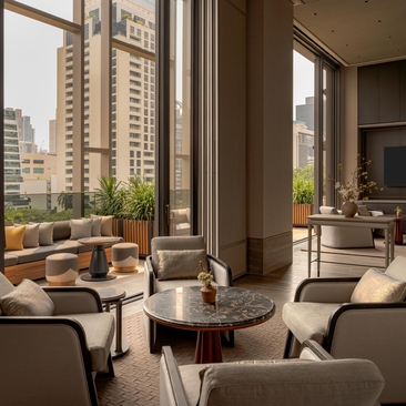 Heritage Room at Aman Nai Lert Bangkok, with floor-to-ceiling windows overlooking the city skyline and comfortable seating.