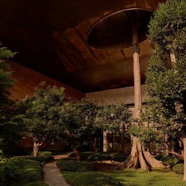 Evening view of Aman Nai Lert Bangkok's exterior with illuminated architectural features and verdant landscaping.