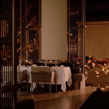 Intimate dining room at Aman Nai Lert Bangkok with soft lighting, wooden screens, and elegantly dressed table.