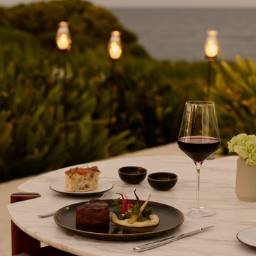 Intimate private dining setting at Amanera resort with plated cuisine, wine, and candlelit garden views at dusk.