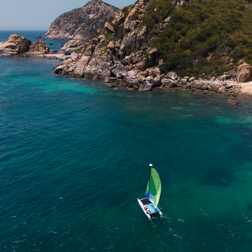 Hobie Cat sailing in turquoise waters off the rocky coast at Amanoi, Vietnam.