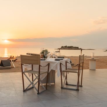 Tavolo da pranzo allestito sulla spiaggia al tramonto, Amanzoe resort in Grecia.