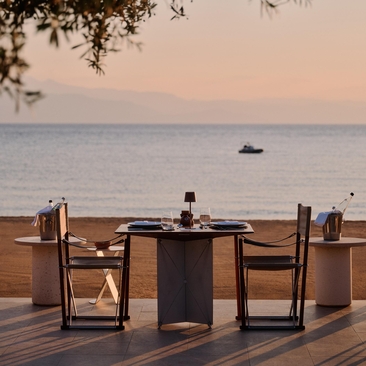 Tavolo da pranzo sulla spiaggia al tramonto presso il Beach Club di Amanzoe, resort in Grecia.
