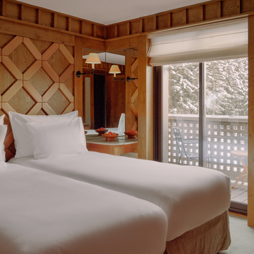 Junior family apartment bedroom at Aman Le Mélézin with twin beds and alpine views through glazed doors.