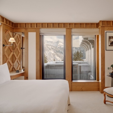 Chambre Nord bedroom at Aman Le Mélézin with wooden panelling, large windows overlooking snowy landscape, and white bed.