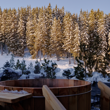 Wooden bath overlooking snow-covered forest at Aman Le Mélézin, French Alps.