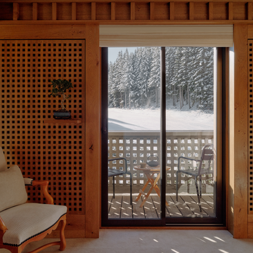 Chambre at Aman Le Mélézin with snowy alpine views through glass doors and terracotta wooden wall panelling.