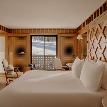 Bedroom at Aman Le Mélézin with twin beds, wooden panelling, and ski slope views through balcony doors.