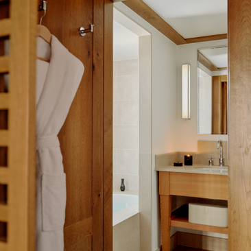 Wooden corridor at Aman Le Mélézin with en-suite bathroom visible, featuring warm timber finishes and towel rail.