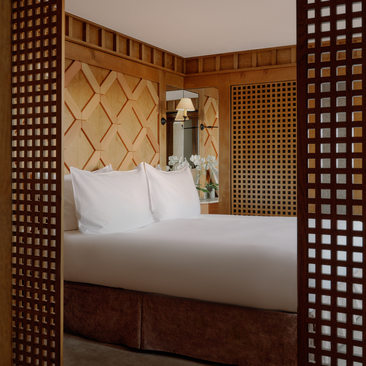 Bedroom at Aman Le Mélézin with wooden lattice screens, quilted headboard and white bedding.