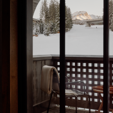 Window seat at Aman Le Mélézin overlooking snowy Alpine landscape through geometric lattice screen.