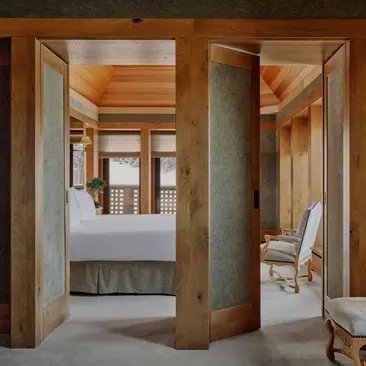 Suite bedroom at Aman Le Mélézin resort with wooden architectural framing and ensuite bathroom.