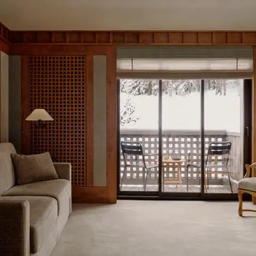 Suite accommodation at Aman Le Mélézin resort overlooking ski piste, with wooden panelling and balcony doors.