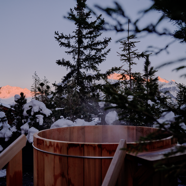 Wooden plunge pool on a terrace at Aman Le Mélézin at dusk, with snowy peaks glowing in the distance.