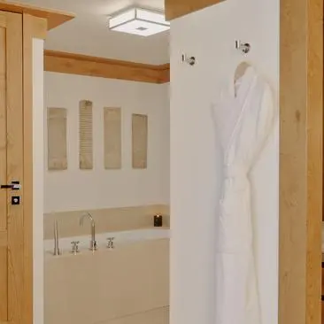 Suite bathroom at Aman Le Mélézin resort with wooden beams, marble bathtub, and towel rail.