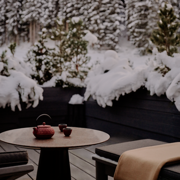Suite with round table overlooking snowy forest and stream at Aman Le Mélézin.
