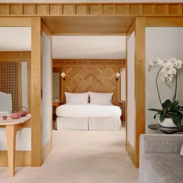 Suite avec lit à baldaquin au resort Aman Le Mélézin, avec boiseries claires et décoration minimaliste.