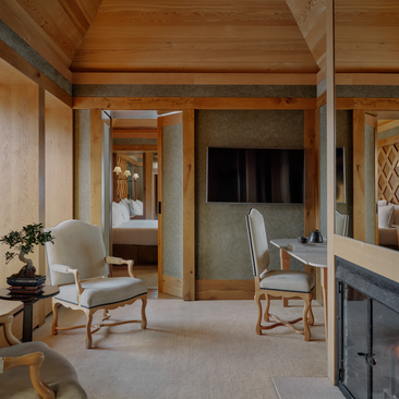 Spacious suite at Aman Le Mélézin with wooden beams, neutral furnishings and multiple rooms leading off a central corridor.