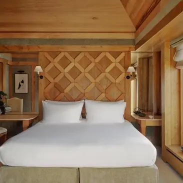 Suite Vanoise bedroom with wooden panelling and white bedding at Aman Le Mélézin resort.