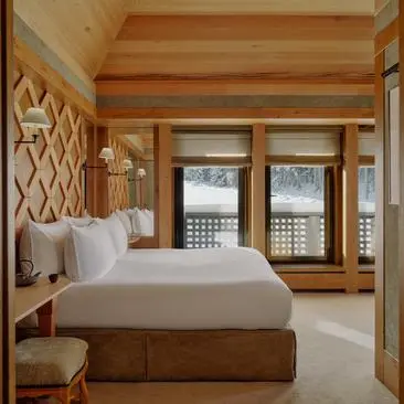 Suite bedroom at Aman Le Mélézin resort with wooden beams, bed and mountain views through glass doors.