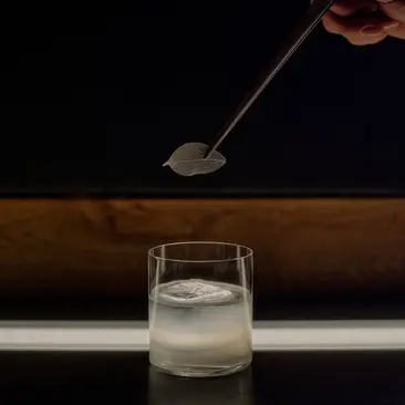 Cocktail being prepared at Aman Le Mélézin resort, with a spoon pouring liquid into a glass.