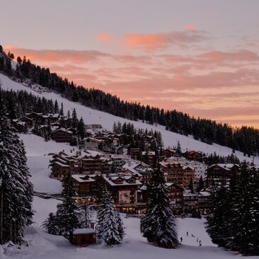 Aman Le Mélézin nestled in snowy French Alps at dusk, with warm golden light across the sky.
