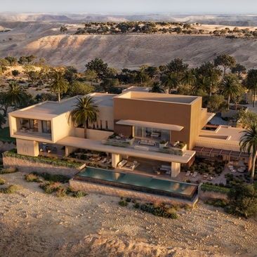 Aerial view of Amansamar's contemporary architecture set amongst palm trees in a desert landscape.